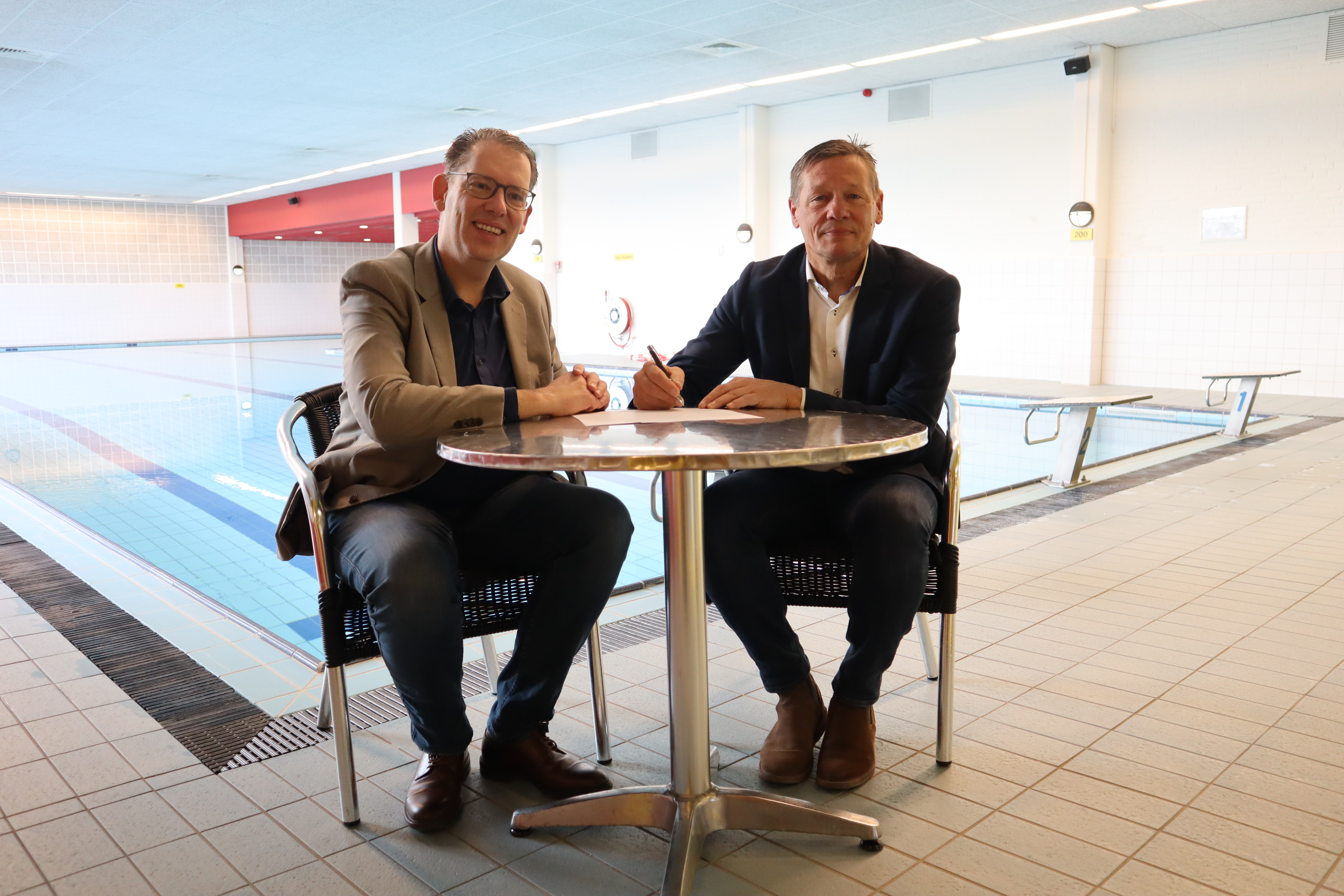 Wethouder Mark Gerritsen (links op de foto) en Winand Willigers, directeur SWEM BV, (rechts op de foto) zetten hun handtekening, met op de achtergrond het binnenzwembad van Eijsden
